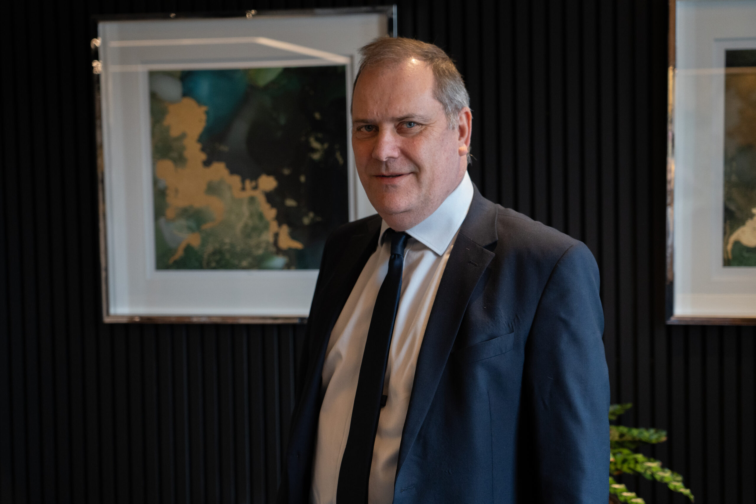 Alastair Sinclair stood up in front of a picture frame on a black wall